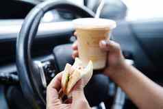亚洲女人司机持有冰咖啡杯三明治面包吃喝车危险的风险事故