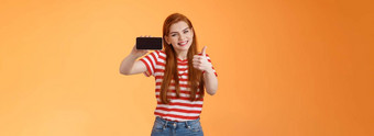 兴奋快乐的红色头发的人有吸引力的女人很高兴显示拇指<strong>介绍</strong>太棒了手机游戏持有智能手机水平微笑批准推荐好在线商店橙色<strong>墙</strong>