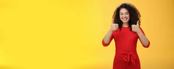 有<strong>创意</strong>的有魅力的快乐乐观的女人卷曲的头发红色的<strong>衣服</strong>眨眼批准显示拇指广泛的微笑满意给积极的回复黄色的墙