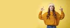 有吸引力的梦幻时尚的大学女孩穿他温暖的毛衣指出前微笑很高兴找到好奇的很酷的促销推荐提供广告复制空间黄色的背景