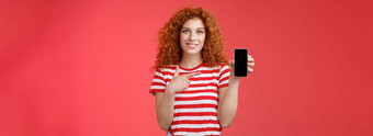 应用程序红色头发的人卷曲的友好的可爱的女孩朋友找到oufit在线商店持有智能手机指出电话屏幕微笑广泛的推荐社会媒体照片过滤器红色的背景