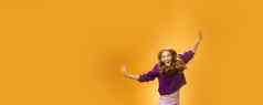 富有表现力的热情的无忧无虑的友好的快乐的红色头发的人女人紫色的毛衣裤子跳快乐提高了手微笑大喊大叫幸福快乐橙色背景