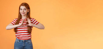 可爱的可爱的快乐的红色头发的人女朋友表达爱珍惜的关系庆祝周年纪念日显示心标志微笑温柔承认同情站橙色背景
