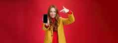 选择电话后悔肖像友善的有吸引力的自信红色头发的人魅力女朋友黄色的外套显示智能手机指出移动微笑广泛的相机