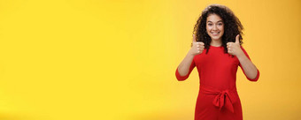 优秀的的想法不错的工作肖像支持很高兴快乐迷人的女朋友显示拇指站红色的衣服黄色的墙微笑给积极的回复喜欢概念