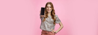 工作室拍摄自信有魅力的年轻的魅力女人介绍太棒了智能手机应用程序显示移动电话显示微笑自信的推荐遵循博主页面站粉红色的背景