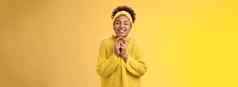 迷人的乐观无忧无虑的年轻的微笑非裔美国人女人关闭眼睛祈祷持有手掌幸福的快乐祝梦想真正的感觉幸运的一天站快乐的黄色的背景