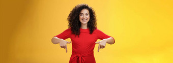 工作室拍摄愉快的微笑年轻的<strong>卷发</strong>女人红色的衣服指出指数手指促进太<strong>棒</strong>了事件微笑广泛的建议买黄色的墙