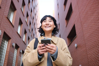 较低的角视图浅黑<strong>肤色</strong>的女人朝鲜文<strong>女孩</strong>听音乐耳机走街智能手机阅读消息移动电话