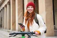 美丽的年轻的女人旅游背包租金e-scooter旅行小镇移动电话应用程序