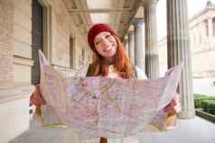 喜欢冒险的红色头发的人女孩走小镇纸地图探讨了城市旅游受欢迎的旅游景点兴奋微笑