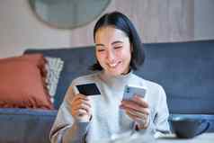 肖像微笑亚洲女人支付信贷卡智能手机应用程序安排直接借记购物在线移动电话