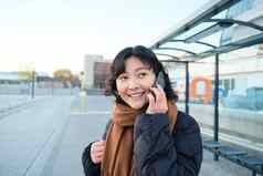 美丽的微笑朝鲜文女孩等待公共汽车停止公共运输会说话的移动电话城市