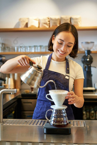 垂直拍摄微笑亚洲酒保咖啡师蓝色的围裙倒水<strong>小水壶</strong>酝酿咖啡计数器咖啡馆