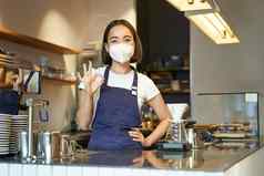 亚洲女咖啡师女孩医疗面具显示标志作品咖啡馆计数器啤酒咖啡作品客户科维德流感大流行