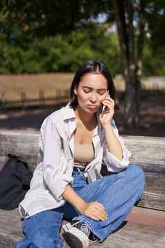 肖像伤心女孩会说话的移动电话生闷气的年轻的女人不安谈话电话坐着板凳上公园心烦意乱脸