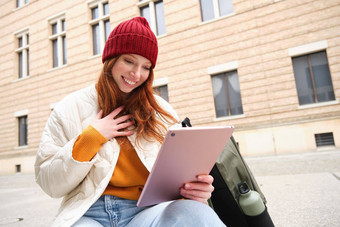 红色头发的人女孩微笑坐在在户外建筑数字平板电脑热水瓶背包连接公共互联网搜索smth在线小工具