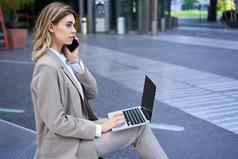 女人会说话的移动电话工作移动PC坐着城市中心街穿西装