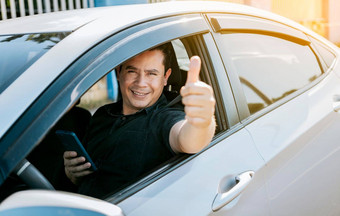 微笑司机持有手机显示拇指司机男人。显示拇指持有手机快乐司机给拇指路安全开车概念