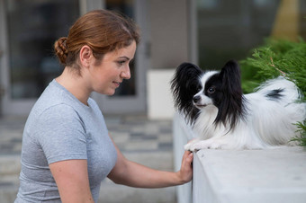 高加索人红发女人拥抱帕皮利翁狗在户外黑色的白色大陆猎犬