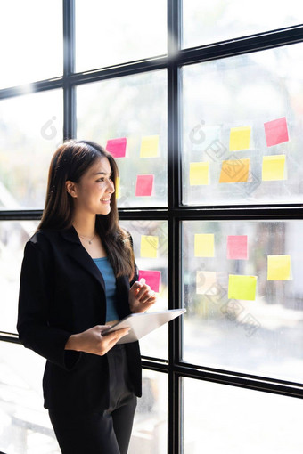 年轻的有创意的女人专业黏糊糊的笔记玻璃墙写作策略业务计划发展成长成功快乐亚洲女人工作办公室