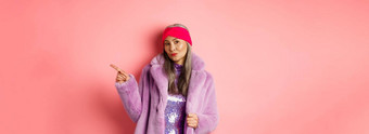 时尚的亚洲高级女人很酷的紫色的冬天外套指出手指显示广告时髦的相机粉红色的背景