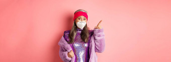 科维德时尚概念惊讶亚洲高级女人闪闪发光的衣服脸面具指出手指上左角落里显示促销提供粉红色的背景