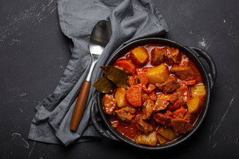 牛肉肉炖肉土豆胡萝卜美味的肉汁黑色的砂锅能湾叶子勺子黑色的黑暗乡村混凝土背景