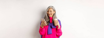 时尚的高级女人喝咖啡智能手机朝鲜文高级夫人阅读消息移动电话微笑白色背景