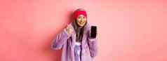 在线购物时尚概念时髦的亚洲高级女人显示空白移动屏幕竖起大拇指推荐互联网促销粉红色的背景