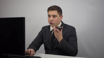 年轻的商人记录的声音消息智能手机男人。西装坐在前面电脑聊天电话