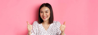 美生活方式概念特写镜头可爱的亚洲女人显示支持使竖起大拇指手势微笑赞美站粉红色的背景