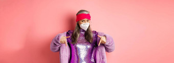<strong>冠</strong>状病毒购物概念时尚的亚洲上了年纪的女人紫色的衣服脸面具指出手指显示促<strong>销</strong>粉红色的背景