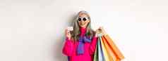 时尚的高级亚洲女人太阳镜购物假期出售持有纸袋塑料信贷卡站白色背景