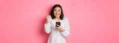 在线购物美概念兴奋亚洲女人赢得互联网持有智能手机欢乐微笑快乐庆祝站粉红色的背景