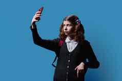 13岁以下的女学生背包采取自拍照片智能手机蓝色的背景