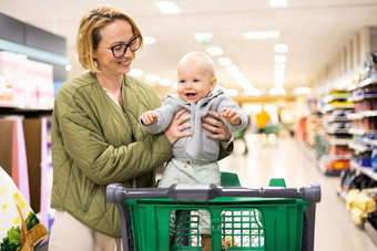 妈妈。推购物车婴儿婴儿男孩孩子部门过道超市杂货店商店购物孩子们概念