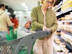 不拘礼节地穿着妈妈。选择产品部门超市杂货店商店婴儿婴儿男孩孩子购物车