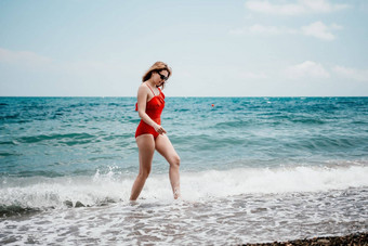 年轻的快乐女人走无忧无虑的海边快乐夫人红色的比基尼肖像美丽的年轻的女人放松微笑海滩海海洋假期假期旅行旅行