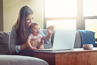 妈妈。婴儿挥舞着移动PC视频调用房子首页生活房间社会距离沟通微笑快乐妈妈孩子女孩沙发变焦技术社会网络说话