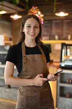 肖像年轻的女咖啡师站前面计数器现代咖啡馆微笑相机