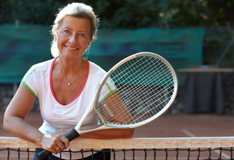 网球感觉伟大的微笑高级女人站网球网持有网拍