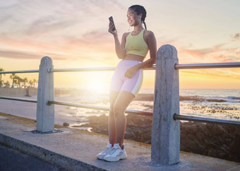 健身海滩女人智能手机运行日落在线流媒体音乐播客自然锻炼跑步者放松滚动社会媒体运行微笑耳机