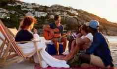 艺人集团男人。玩吉他坐着海滩朋友