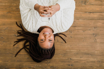 积极的年轻的非洲美国女人聊天手机微笑地板上首页快乐的年轻的女人沟通智能手机在室内