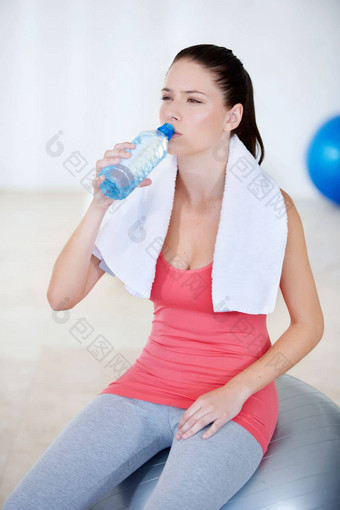 采取sip年轻的女人坐着健身房球喝水