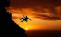 日落天空绕绳下降山轮廓徒步旅行男人。挂影子绳子健身风险冒险自由挑战强大的超现实主义的自然肾上腺素悬崖攀爬橙色景观