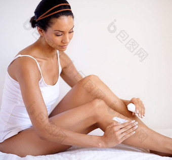 黑色的女人腿保湿霜护肤品化妆品爱护理放松首页床上非洲美国女人应用乳液健康的软光滑的皮肤腿卧室