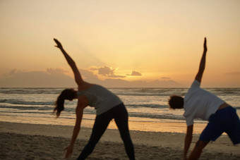 采取护理的身体瑜伽夫妇瑜伽海滩日落