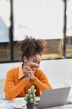 快乐的非洲美国女人坐着户外咖啡馆使视频调用移动PC